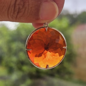 Puede incluir: Un colgante redondo de vidrio facetado naranja con un engaste plateado.