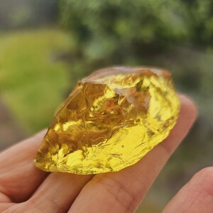 May include: A large, yellow, translucent, irregularly shaped piece of glass. The glass has a rough, textured surface and is being held in a hand.