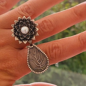 Puede incluir: Dos anillos de plata, uno con un diseño de flor y una perla en el centro, y el otro con un diseño de hoja.