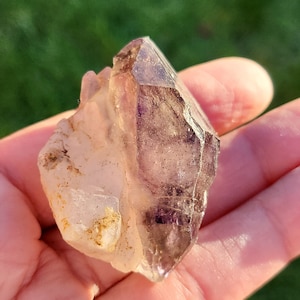 May include: A clear quartz crystal with a purple amethyst point. The crystal is rough and has a natural, raw appearance.