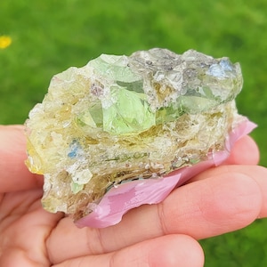 Puede incluir: Un cúmulo de cristales verdes y amarillos con una apariencia translúcida y vidriosa. Los cristales están incrustados en una matriz de material blanco y gris.