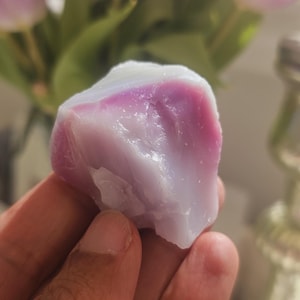 May include: A close-up of a purple and white agate stone. The stone is smooth and polished, with a natural, organic shape.