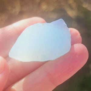 Puede incluir: Un cristal blanco translúcido con un ligero tono azul, sostenido en una mano.