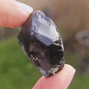 Könnte beinhalten: Ein schwarzer Obsidian-Stein mit einer glänzenden, glasartigen Oberfläche. Der Stein hat ein einzigartiges, wirbelndes Muster aus weißen und grauen Einschlüssen.