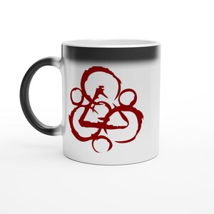 Può includere: Tazza in ceramica bianca con manico nero. La tazza presenta un design astratto rosso sul davanti. Il design è composto da forme interconnesse, tra cui cerchi e un triangolo. La tazza è progettata per bevande calde.