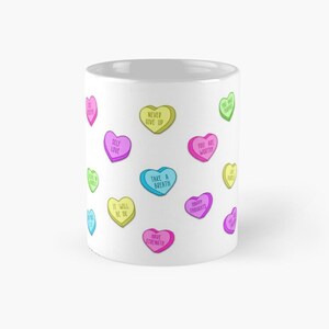 May include: White ceramic mug decorated with colorful heart-shaped candies. Each candy has a different positive message, such as "Self Love," "Never Give Up," and "You Are Worthy." The mug is a cheerful and uplifting gift.
