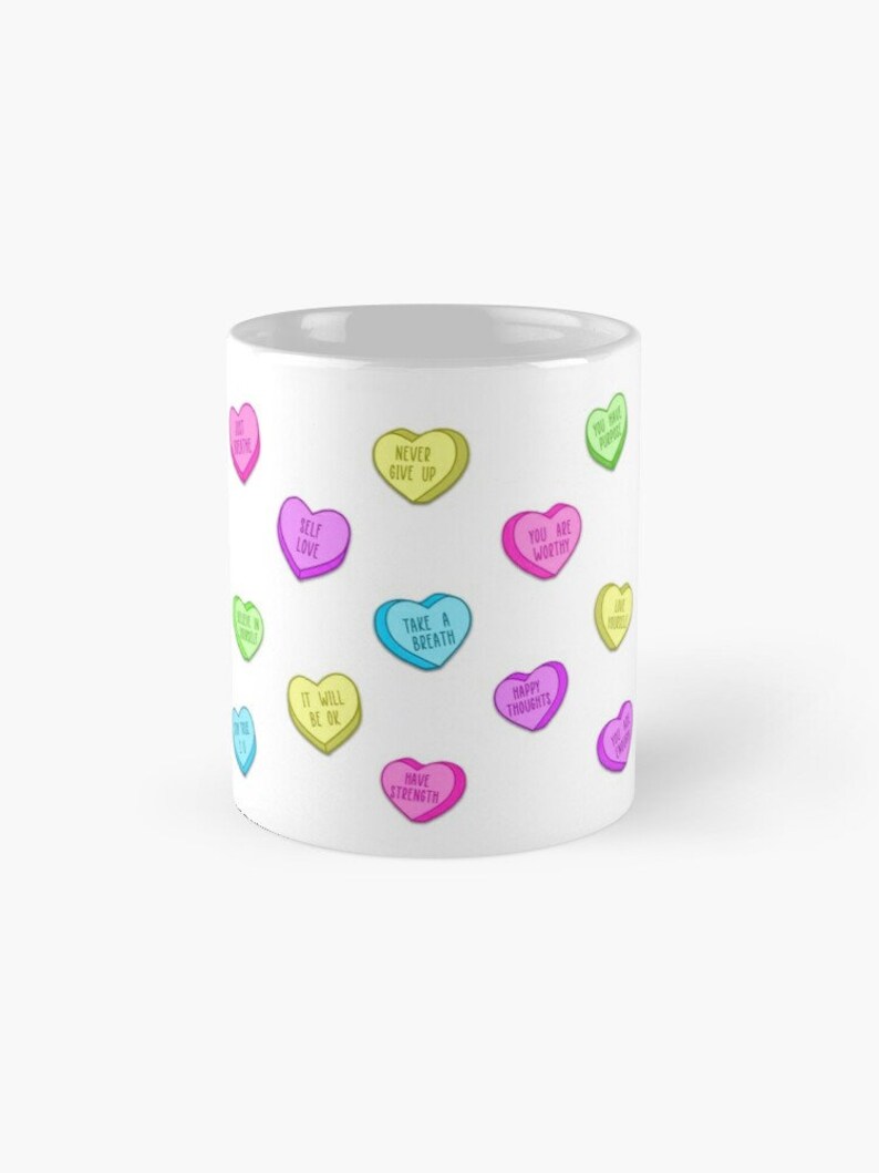 May include: White ceramic mug decorated with colorful heart-shaped candies. Each candy has a different positive message, such as "Self Love," "Never Give Up," and "You Are Worthy." The mug is a cheerful and uplifting gift.