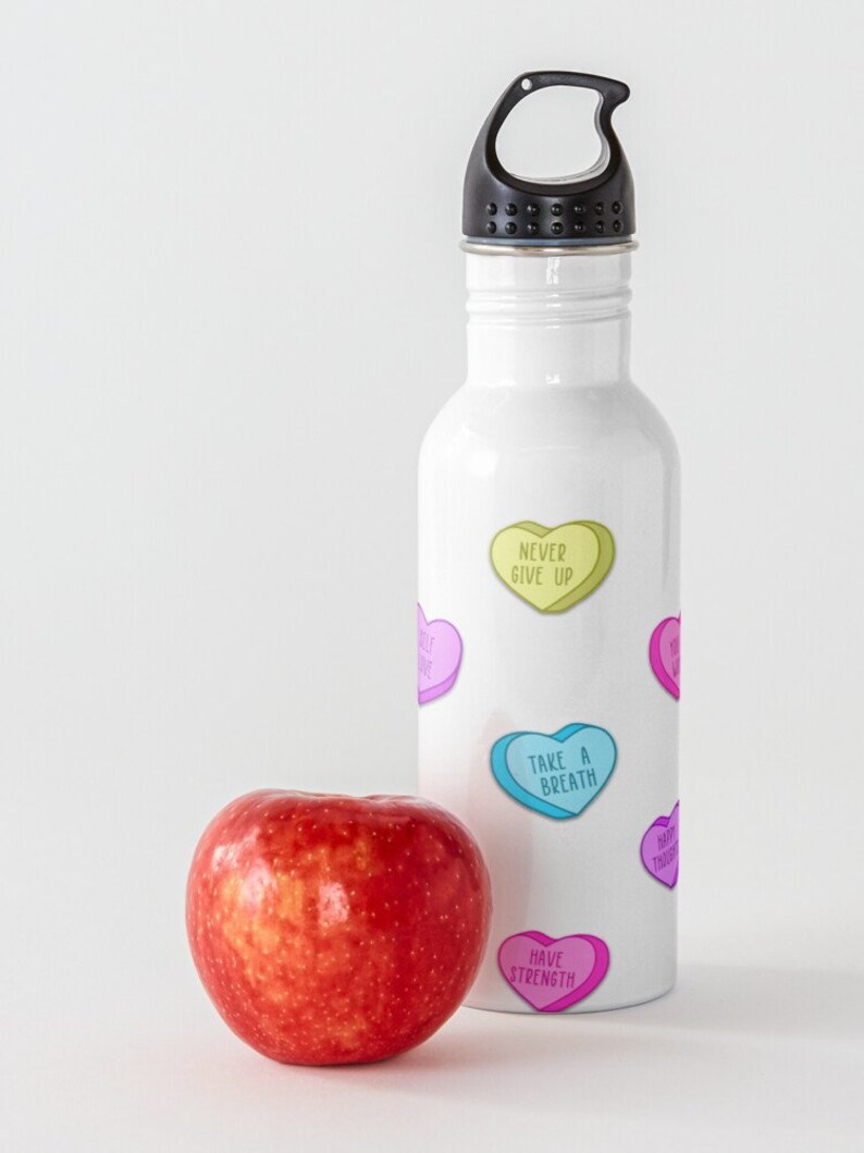 May include: A white water bottle with a black cap and colorful heart-shaped graphics with motivational phrases. A red apple sits next to the bottle. The phrases include "Never Give Up" and "Take a Breath".