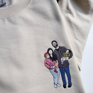Puede incluir: Sudadera beige con un retrato familiar bordado. El retrato representa a una familia de cuatro, con dos adultos y dos ni&ntilde;os. La familia viste varios colores, incluyendo rosa, azul y negro.