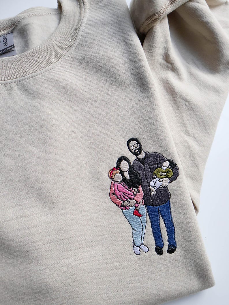Puede incluir: Sudadera beige con un retrato familiar bordado. El retrato representa a una familia de cuatro, con dos adultos y dos ni&ntilde;os. La familia viste varios colores, incluyendo rosa, azul y negro.
