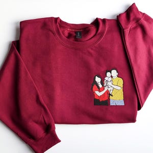 Puede incluir: Una sudadera burdeos con cuello redondo y mangas largas. Un parche bordado en la parte delantera representa a una familia de tres. La familia est&aacute; compuesta por una mujer con camisa roja, un hombre con camisa amarilla y un ni&ntilde;o.