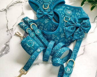 Könnte beinhalten: Ein blaues Hundegeschirr in Teal mit einer passenden Leine und einem Kotbeutelhalter. Das Geschirr und die Leine haben ein Blumenmuster mit dem Text "Wild Cub" auf der Schnalle.