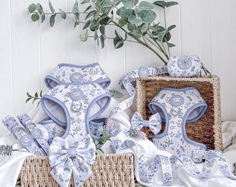 May include: A set of four floral dog harnesses in a light blue and white pattern with a matching bow tie. The harnesses are made of soft, comfortable fabric and are perfect for everyday wear. The harnesses are displayed on a wicker basket with a white background.