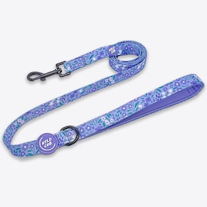 May include: A purple and green floral dog lead with a matching collar. The lead has a black metal clip and the collar has a purple button with the text "WYLD CUB".