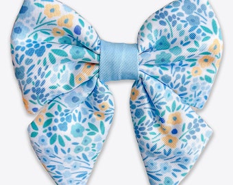 May include: A blue and white floral bow with a light blue center. The bow is made of fabric and has a delicate floral pattern.