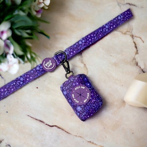 May include: Purple dog leash with a floral pattern and a matching purple poop bag holder with the text "WYLD CUB" on it.