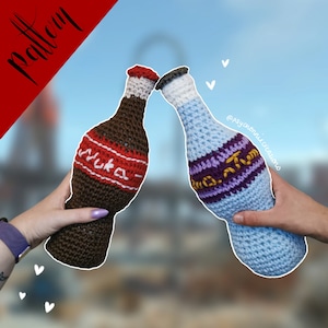 Puede incluir: Dos botellas de soda de crochet, una marrón con la inscripción "Nuka Cola" y la otra azul con una etiqueta morada y dorada.