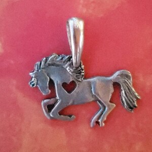 May include: A silver horse charm with a heart cut-out. The horse is in a running pose with its mane flowing.