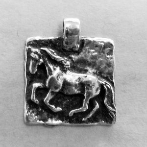 May include: A silver pendant featuring a detailed, textured design of a horse running. The pendant has a square shape with a loop at the top for attaching a chain.