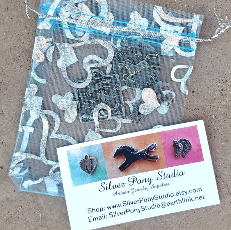 May include: A business card for Silver Pony Studio, an artisan jewelry supply shop. The card features a silver horse charm, a silver heart charm, and a silver horse head charm. The card also includes the shop's website and email address.