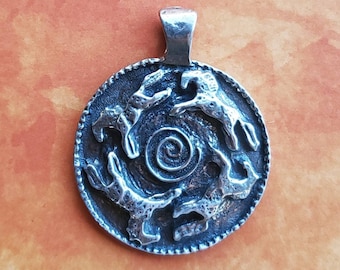 May include: A silver pendant featuring four stylized horses running in a circle around a spiral design. The pendant is on a brown background.
