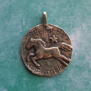 May include: Silver pendant with a horse design and the words "Attempt the impossible" engraved on it.