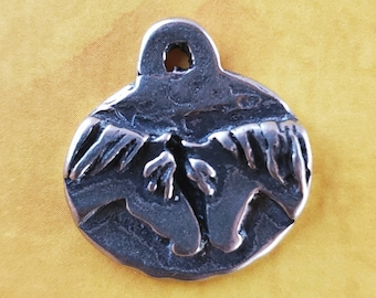 May include: A silver charm featuring two horses' heads facing each other, with their manes flowing in the wind. The charm has a loop at the top for attaching to a necklace or bracelet.