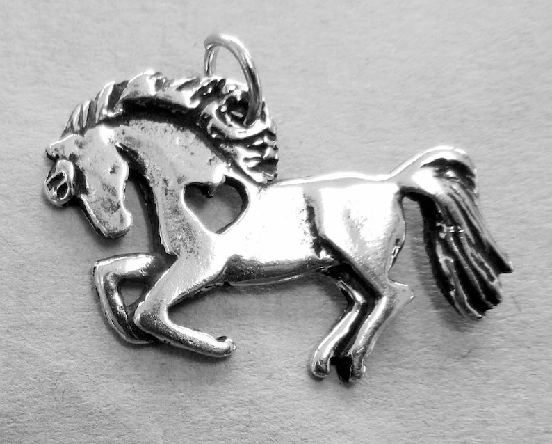May include: Silver charm of a horse with a heart cut out of its body. The horse is running with its mane flowing in the wind.
