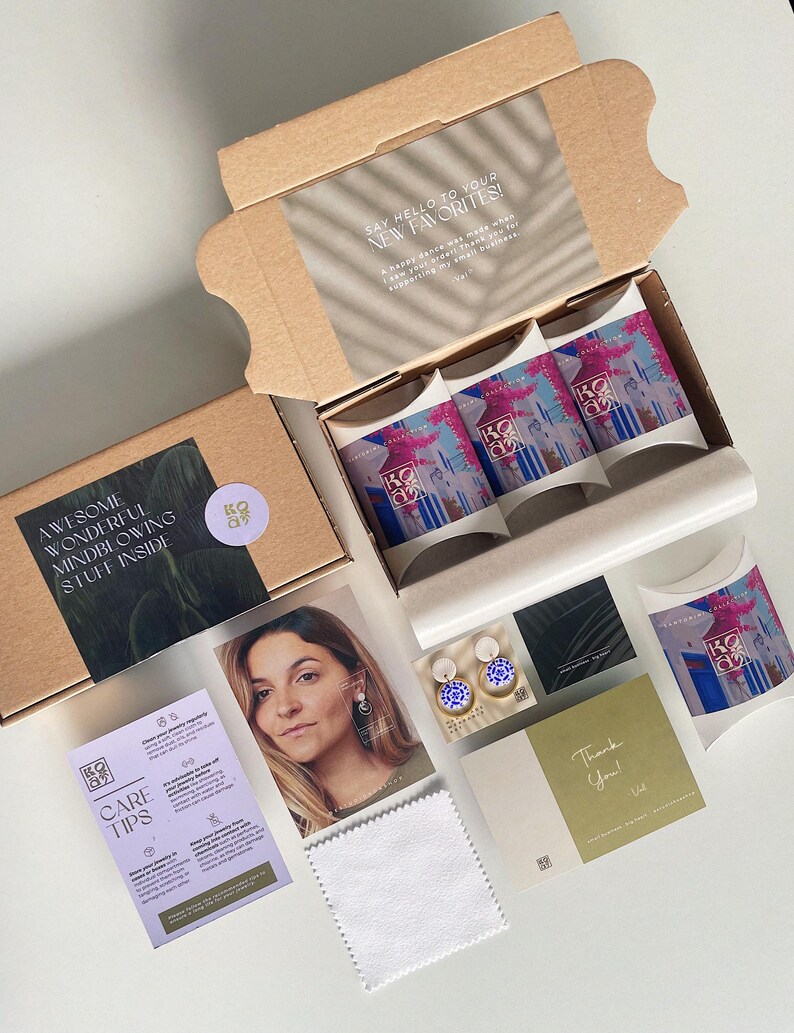May include: A cardboard box, open to reveal packaged products, including three boxes with colourful designs. Other items include a photo, care tips, a thank you card, and a cleaning cloth. Text includes "Say Hello to Your New Favorites!" and "Awesome Wonderful Mindblowing Stuff Inside."