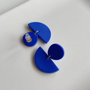 K&ouml;nnte beinhalten: Ein Paar blaue geometrische Ohrringe mit einer Halbkreis- und einer Kreisform. Die Ohrringe sind aus Polymer Clay gefertigt und haben einen silbernen Stift.