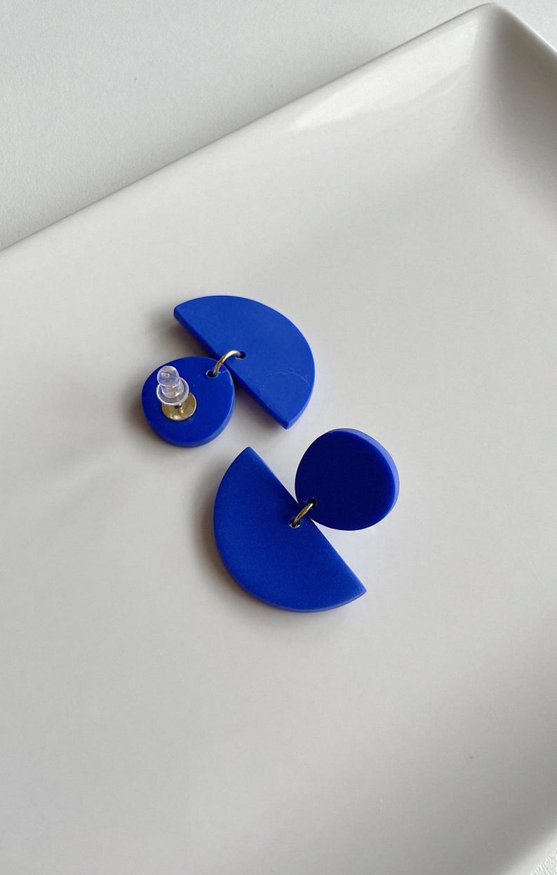 K&ouml;nnte beinhalten: Ein Paar blaue geometrische Ohrringe mit einer Halbkreis- und einer Kreisform. Die Ohrringe sind aus Polymer Clay gefertigt und haben einen silbernen Stift.