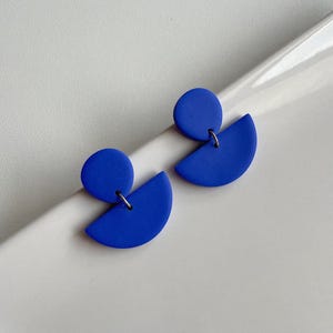 K&ouml;nnte beinhalten: Ein Paar blaue geometrische Ohrringe mit einer Kreis- und einer Halbkreisform.