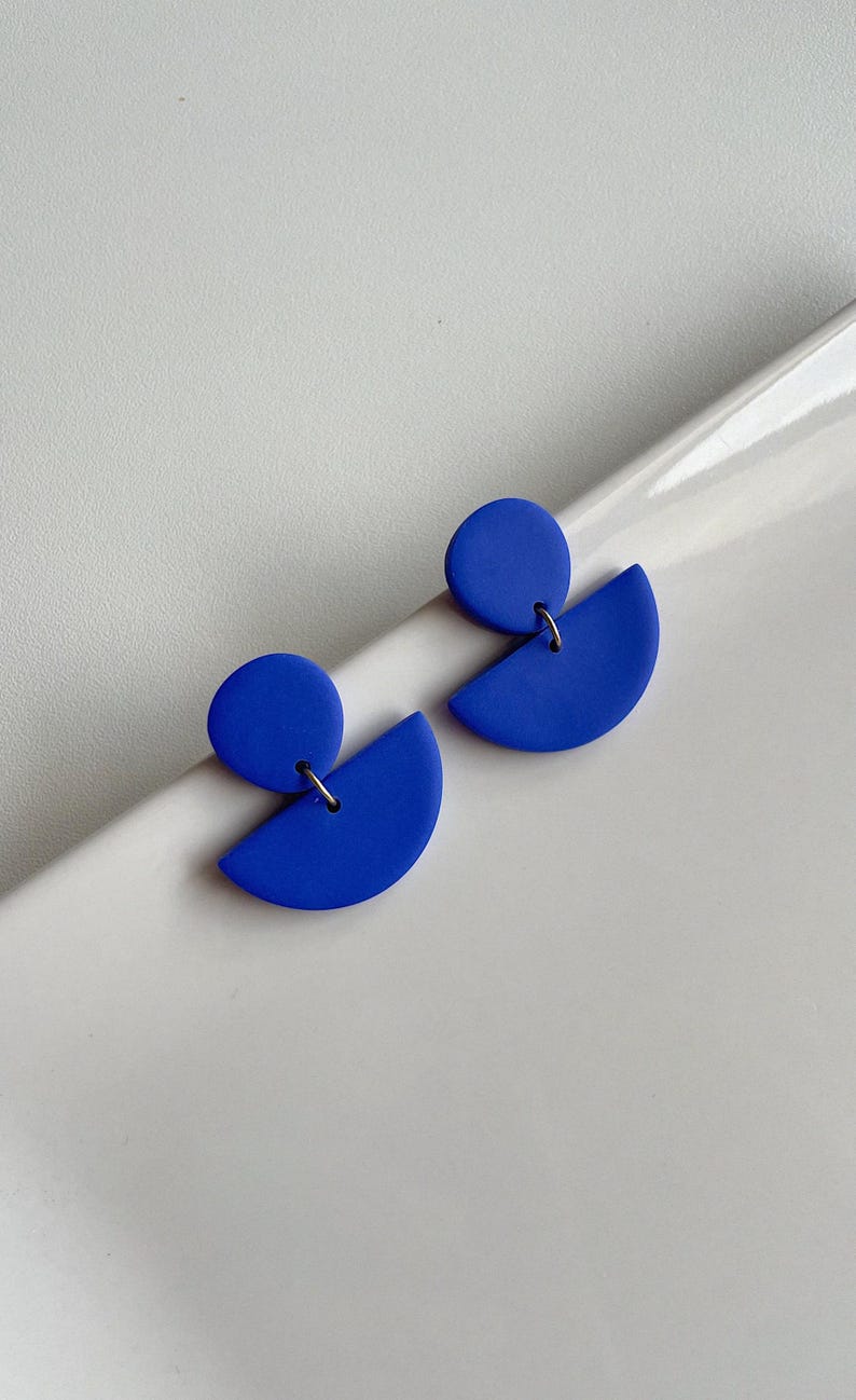 K&ouml;nnte beinhalten: Ein Paar blaue geometrische Ohrringe mit einer Kreis- und einer Halbkreisform.