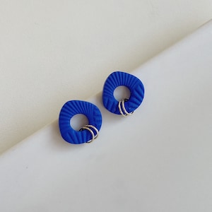 Könnte beinhalten: Ein Paar blaue geometrische Ohrringe mit strukturierter Oberfläche und goldenen Ringen.