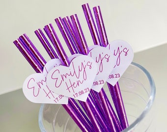 May include: Purple and silver striped paper straws with white heart-shaped tags that say "Emily's Hen 17.08.23" and "Emily's 17.08.23" in pink cursive writing. The straws are in a clear glass vase.