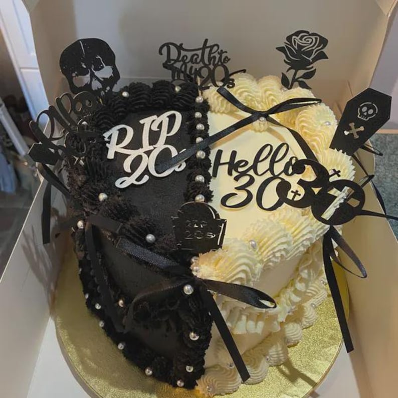 May include: A two-toned cake, half black and half cream, decorated with black and silver accents. The black side says "RIP 20s" and the cream side says "Hello 30". Toppers include a skull, rose, and coffin.