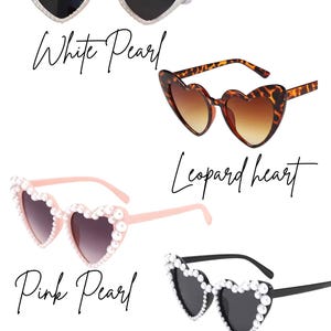 May include: Four pairs of heart-shaped sunglasses in various styles. The options include white pearl, leopard print, pink pearl, and black pearl designs. Each pair has dark lenses and is displayed against a white background.