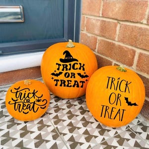 May include: Three orange pumpkins with black "Trick or Treat" lettering and Halloween-themed graphics. The pumpkins are of varying sizes and are displayed on a patterned tile surface, perfect for Halloween decorations.