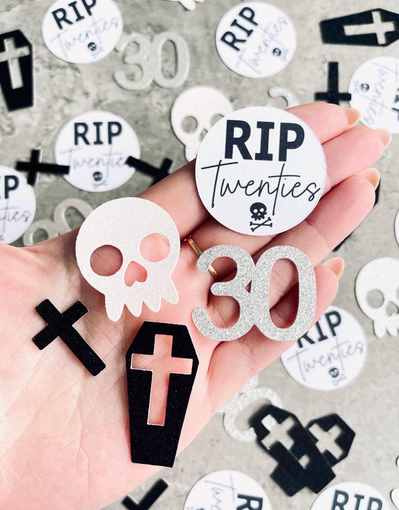 May include: A collection of black and silver glitter confetti featuring a skull, cross, coffin, and the words "RIP Twenties" and "30".