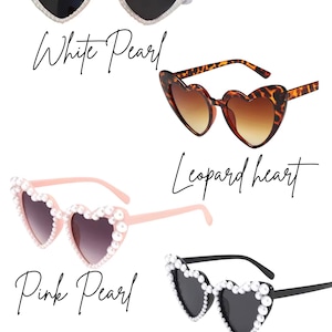 May include: Four pairs of heart-shaped sunglasses in various styles. The options include white pearl, leopard print, pink pearl, and black pearl designs. Each pair has dark lenses and is displayed against a white background.