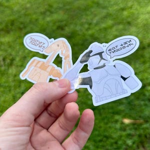 May include: Two Star Wars stickers. One sticker features a white and gray clone trooper saluting with the text "Good job, you did it!" in a speech bubble. The other sticker features a beige droid with the text "Good job, you did it!" in a speech bubble.