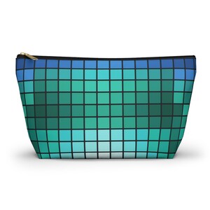 May include: A rectangular cosmetic bag with a blue, teal, and green pixelated design. The bag has a black zipper and a gold-colored zipper pull. The bag is a light color and stands upright on a white surface.