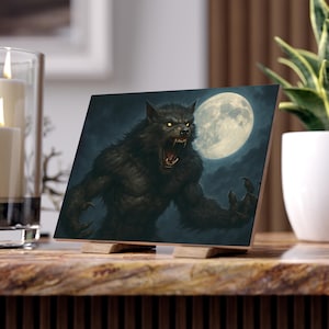 May include: A square wooden art print shows a snarling werewolf with glowing yellow eyes against a full moon in a dark, cloudy sky. The werewolf is dark grey with sharp claws. The print is displayed on a wooden stand.