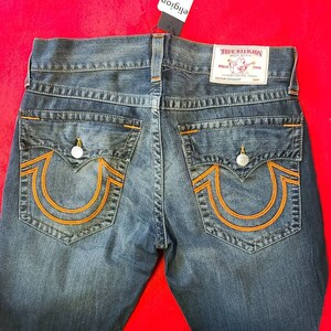 Puede incluir: Vaqueros de mezclilla azul con costuras naranjas y dise&ntilde;o de bolsillo de herradura. Los vaqueros tienen una etiqueta True Religion y cierre de bot&oacute;n. Los vaqueros son de corte recto.