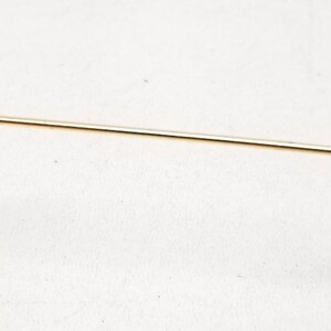 May include: A gold-colored metal arm of a pair of glasses with a brown leather tip.