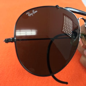 Puede incluir: Gafas de sol aviador Ray-Ban negras con lentes marrones. Las gafas se reflejan en los lentes.