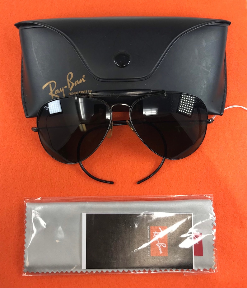 Puede incluir: Gafas de sol aviador Ray-Ban negras con una funda negra y un pa&ntilde;o de limpieza gris. Las gafas de sol tienen un logotipo Ray-Ban dorado en la funda y un logotipo Ray-Ban dorado en el pa&ntilde;o de limpieza.