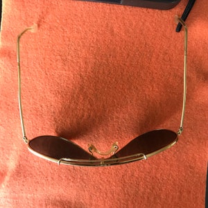 May include: Gold aviator sunglasses with brown lenses. The sunglasses are folded in half and the arms are bent back.