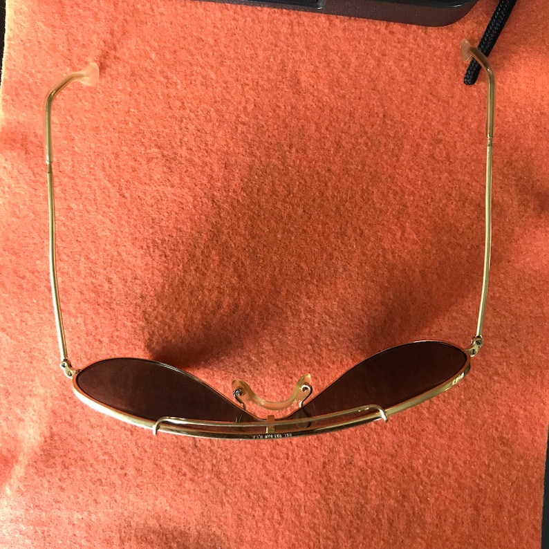 May include: Gold aviator sunglasses with brown lenses. The sunglasses are folded in half and the arms are bent back.