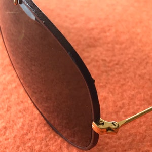 Op de afbeelding: Close-up van het scharnier van een paar gouden aviator-zonnebrillen met zwarte monturen en donkere glazen.